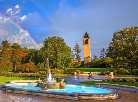 Iowa State University campanile behind fountain and a rainbow in the sky.